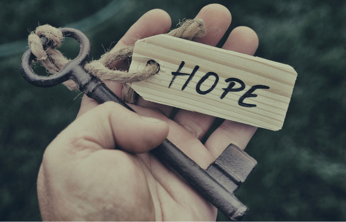 A hand holding an antique key with a wooden tag reading HOPE